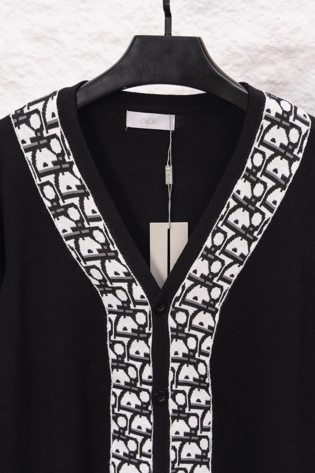 Black V-neck sweater with white patterned trim and button placket, on hanger