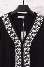 Black V-neck sweater with white patterned trim and button placket, on hanger