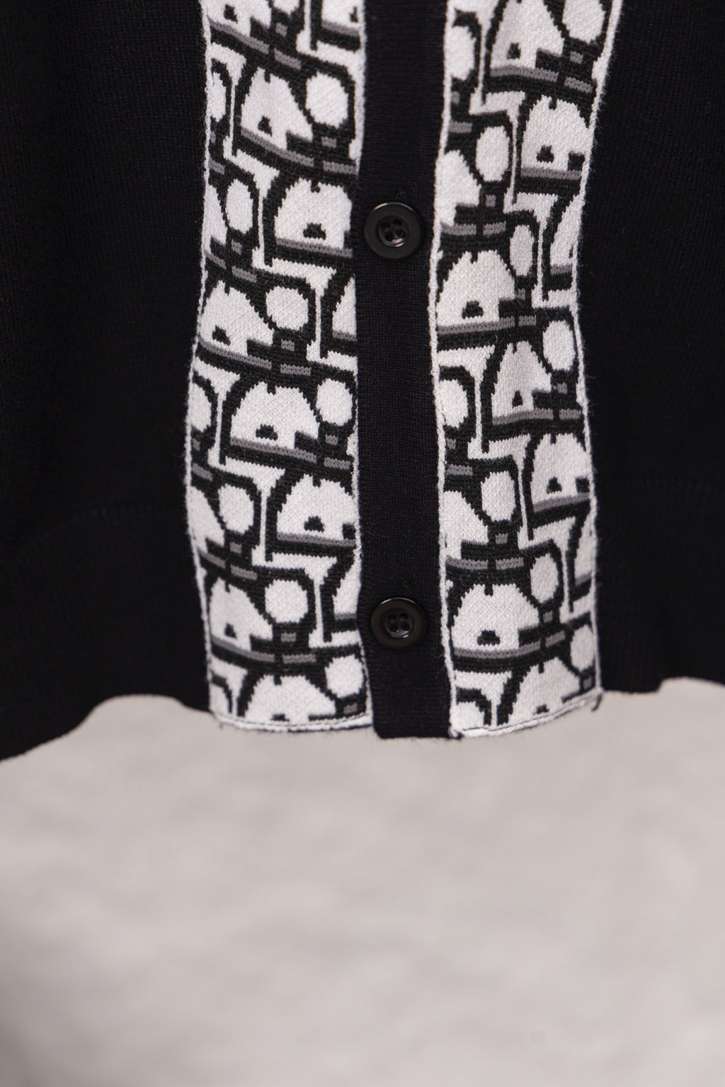 Black sweater hem detail with white patterned front panel and two buttons