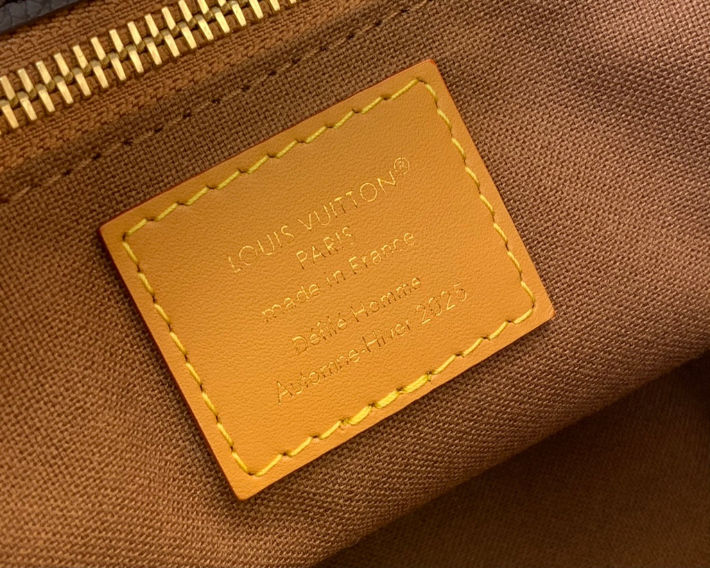 Leather interior tag with Louis Vuitton text and gold stitching.