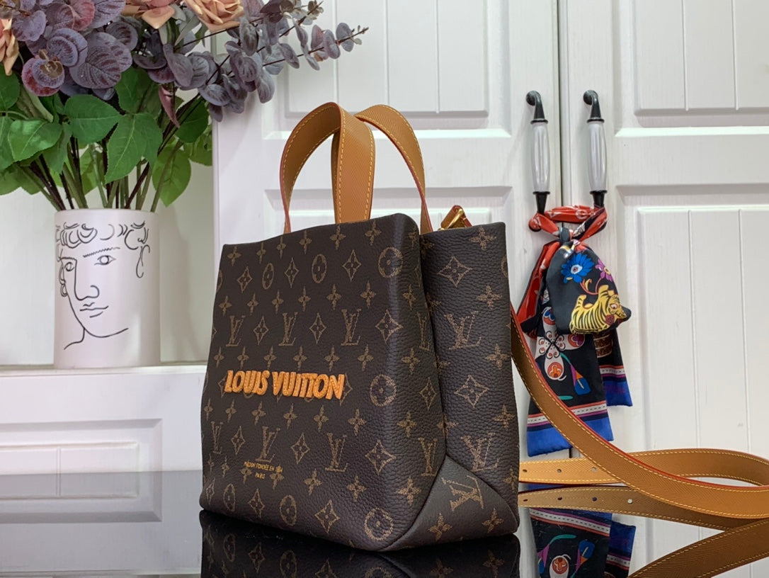 Tote bag in brown monogram canvas with tan top handles and shoulder strap.