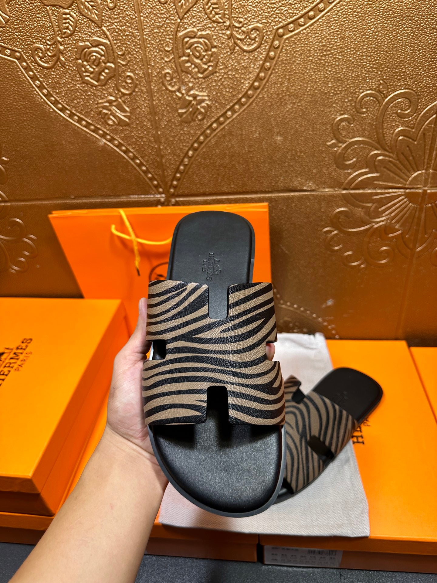 Hand holding black slide sandals with zebra-striped straps, showing top view.