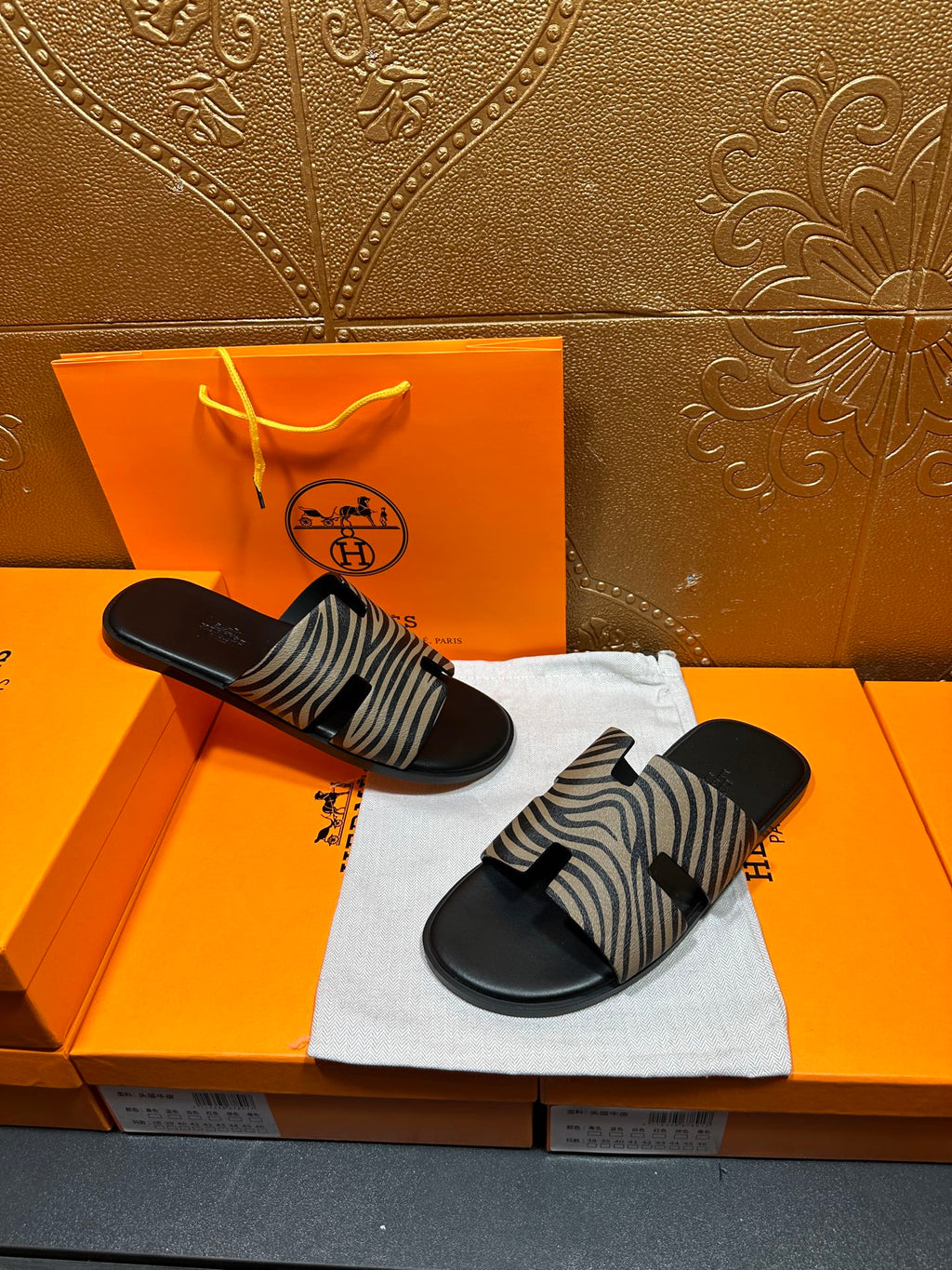 Black slide sandals with zebra-striped straps, pair resting on white cloth.