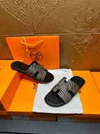 Black slide sandals with zebra-striped straps, pair resting on white cloth.