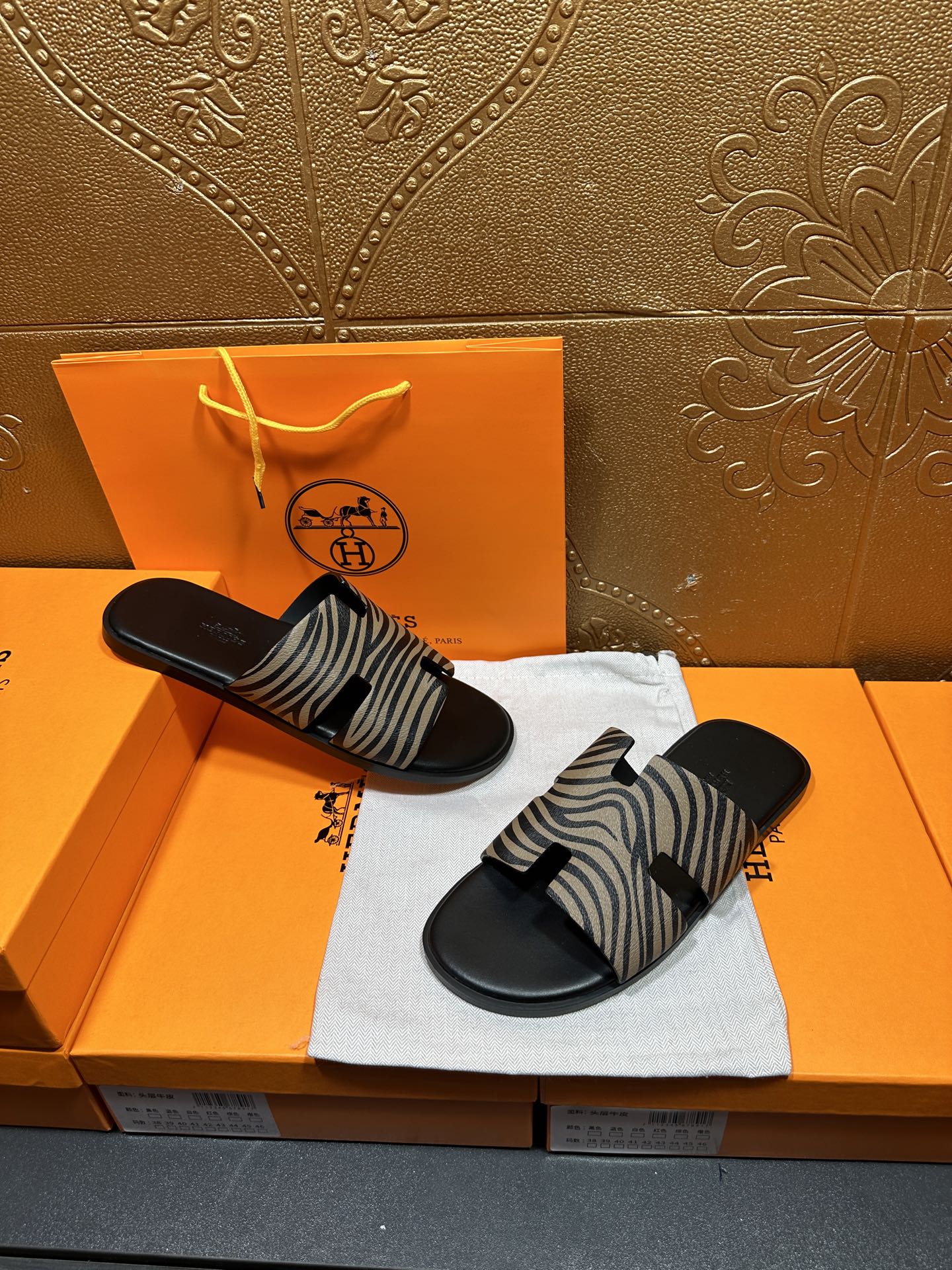 Black slide sandals with zebra-striped straps, pair resting on white cloth.