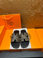 Black slide sandals with zebra-striped straps, shown side-by-side on cloth bag.