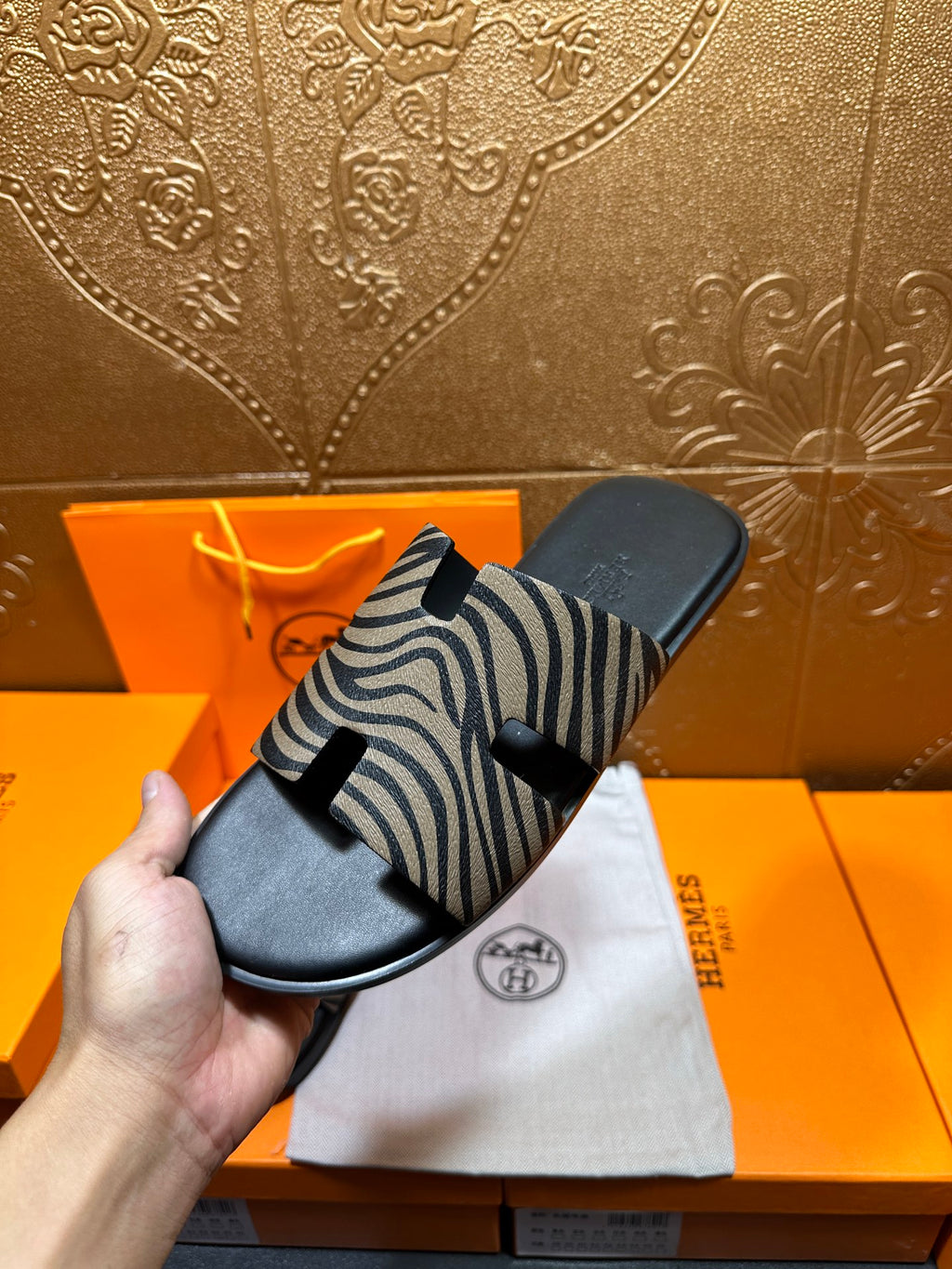 Hand holding black slide sandals with zebra-striped straps, close-up angle.