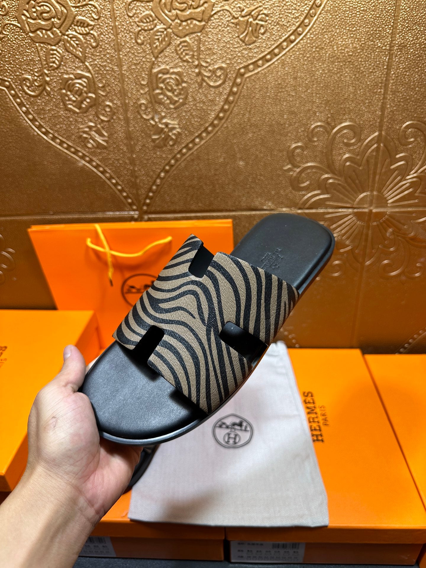 Hand holding black slide sandals with zebra-striped straps, close-up angle.