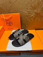 Black slide sandals with zebra-striped straps on white cloth, angled view.