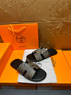 Black slide sandals with zebra-striped straps, angled on white cloth pad.