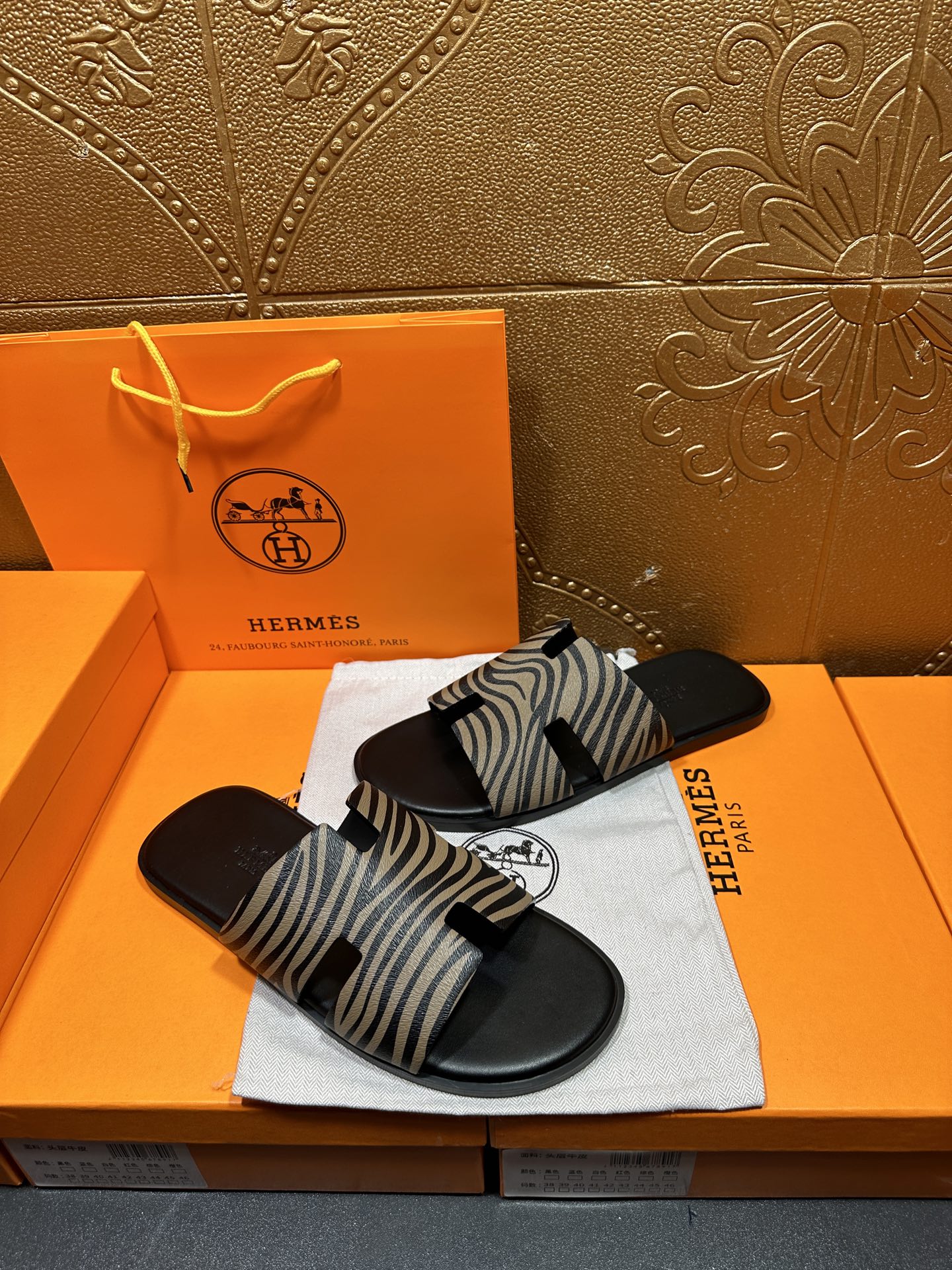 Black slide sandals with zebra-striped straps, angled on white cloth pad.