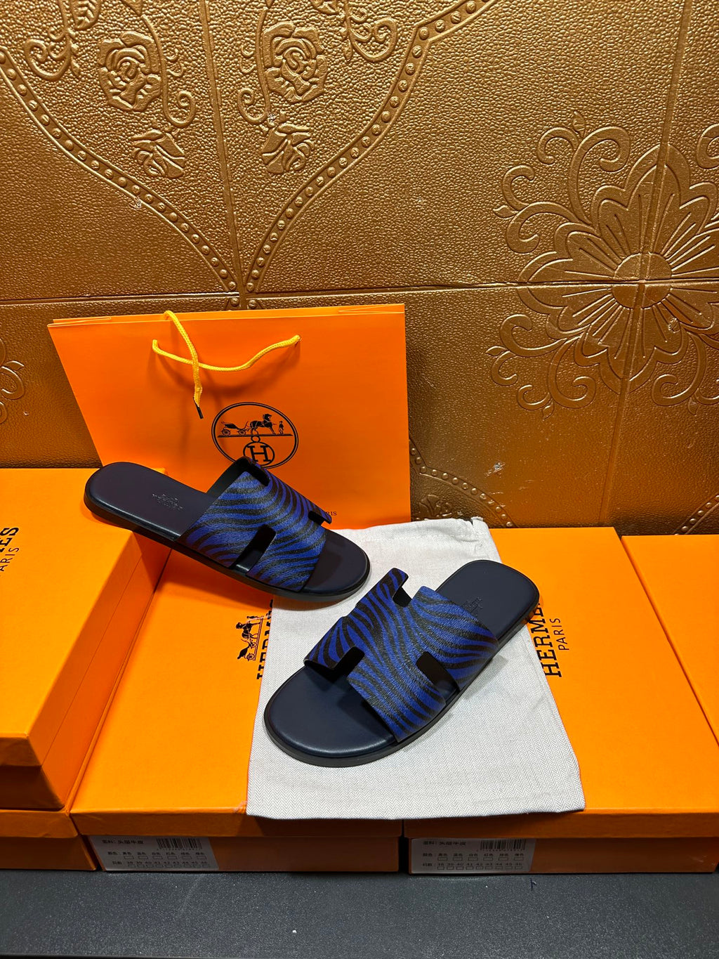 Blue patterned slide sandals held in hand, black strap detail