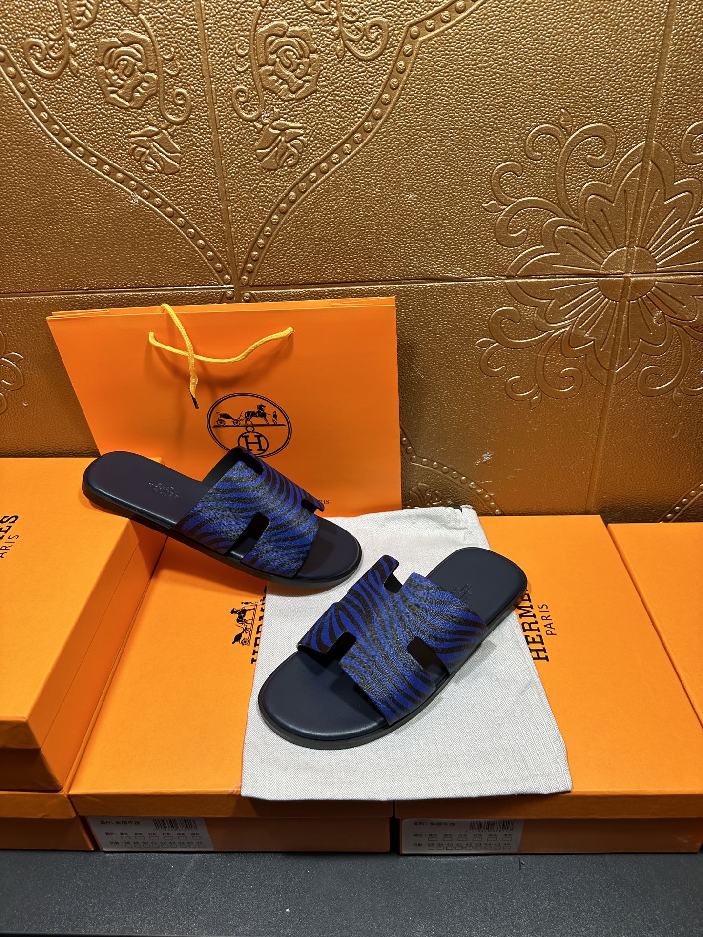 Blue patterned slide sandals held in hand, black strap detail