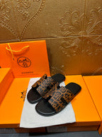 Pair of leopard-print slide sandals with black footbed and straps, shown at an angle.