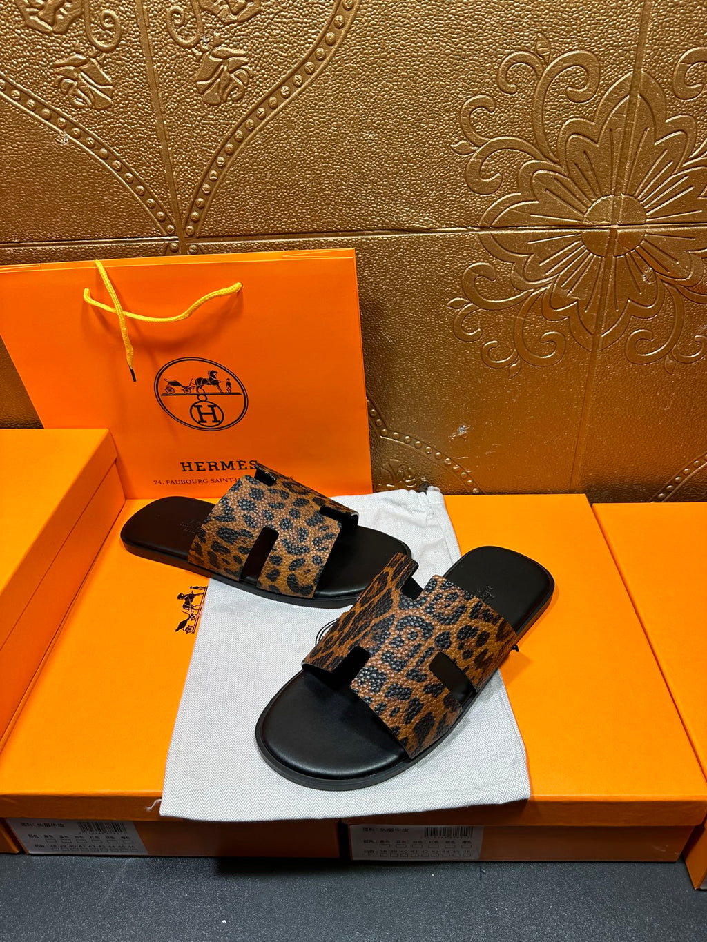 Leopard-print slide sandals with black footbed, angled view over a white dust bag.