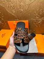 Hand holding leopard-print slide sandal with black sole and thick wide strap, side view.