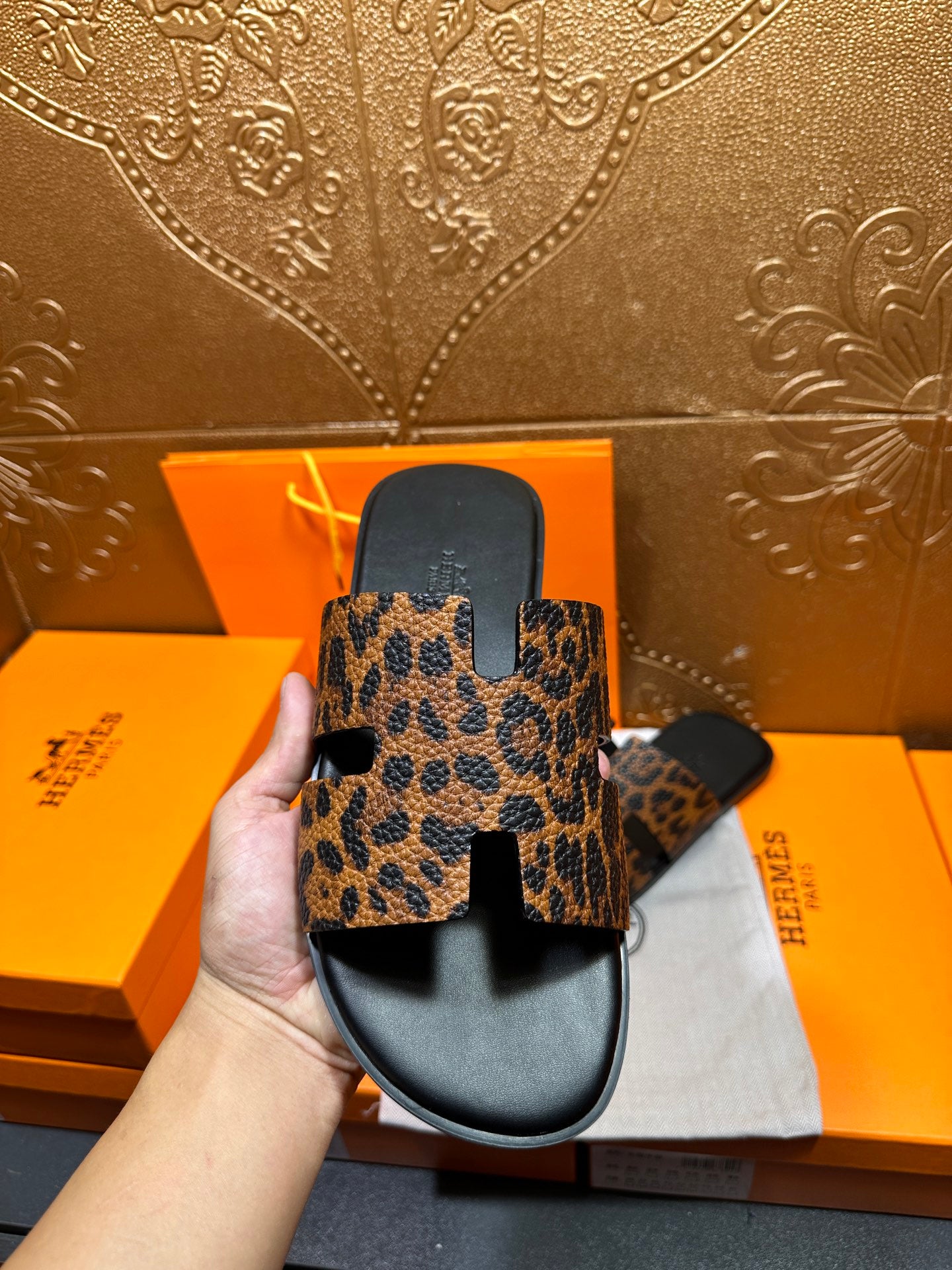Hand holding leopard-print slide sandal with black sole and thick wide strap, side view.