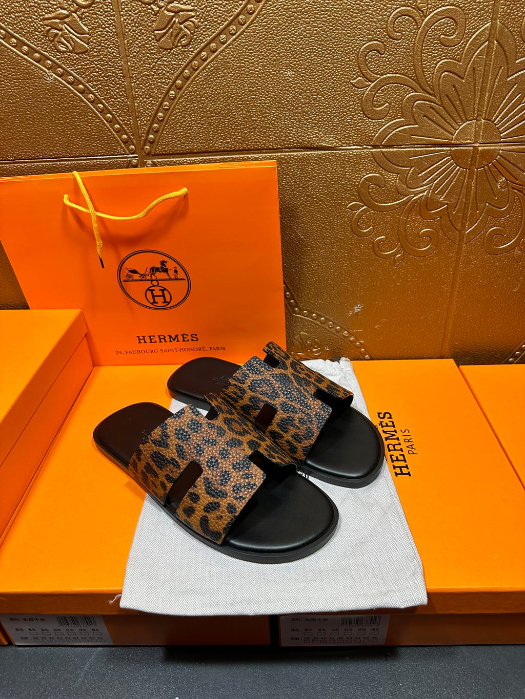 Leopard-print slide sandals with black rubber soles and wide strap across toes, on dust bag.