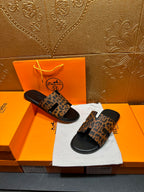 Leopard-print slide sandals with black soles, arranged on dust bag beside orange boxes.