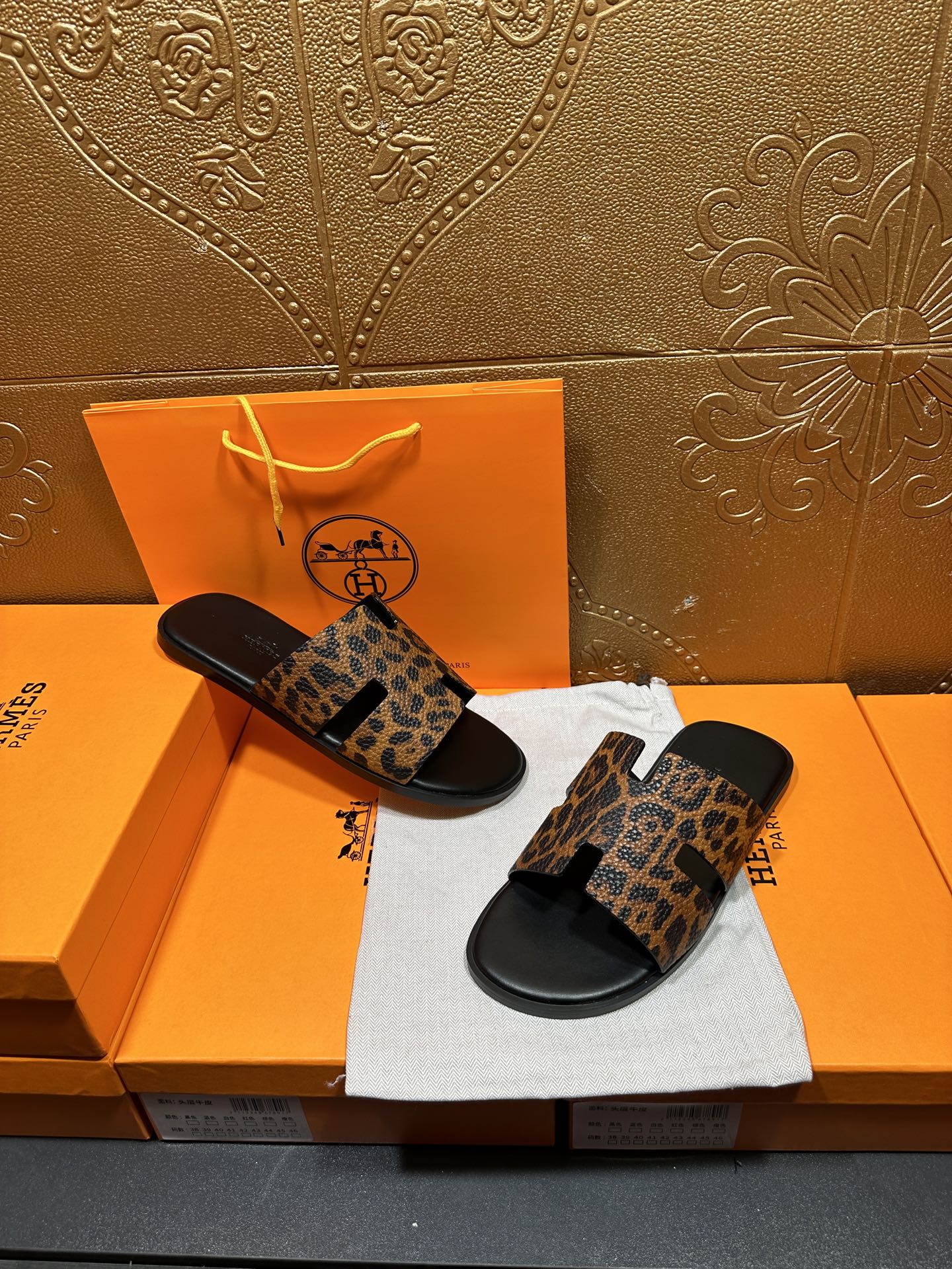 Leopard-print slide sandals with black soles, arranged on dust bag beside orange boxes.
