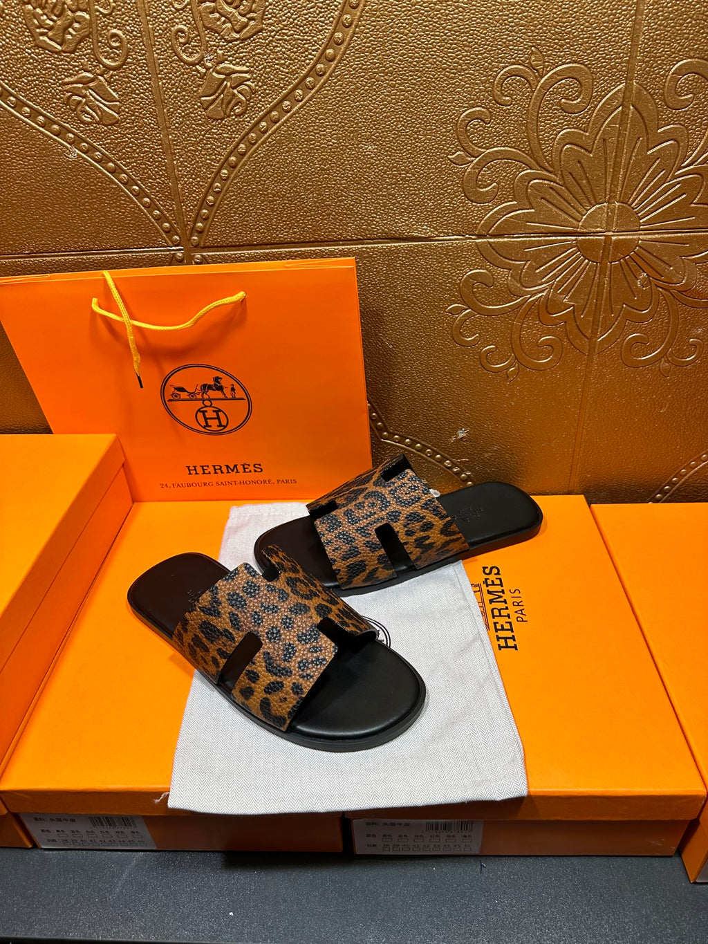 Leopard-print slide sandals with black rubber sole, placed on white cloth atop orange box.