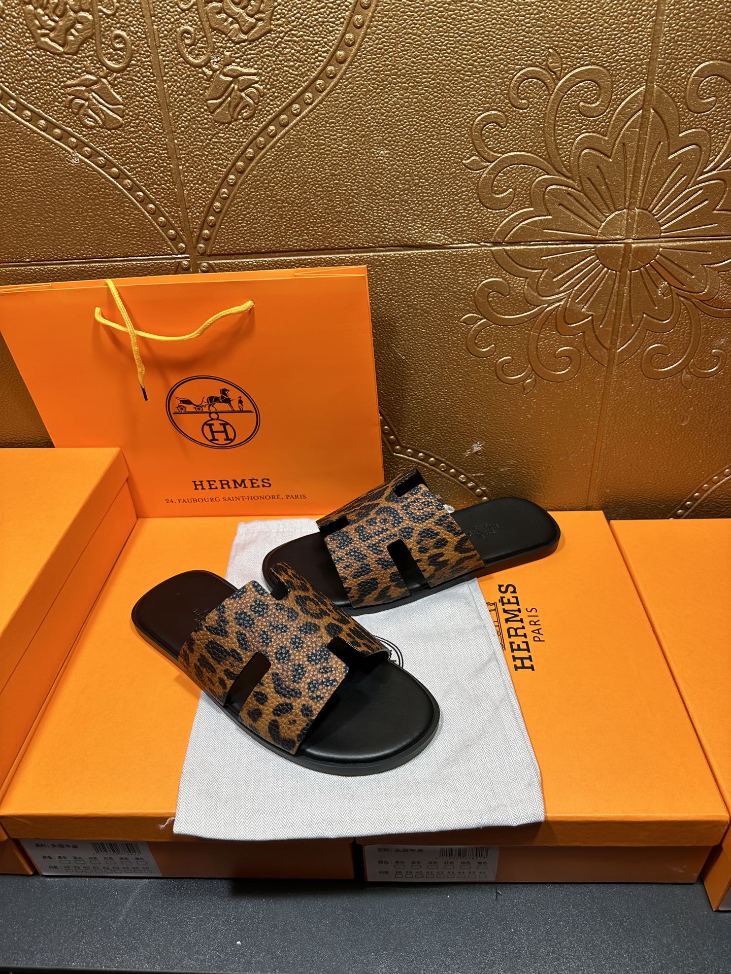 Leopard-print slide sandals with black rubber sole, placed on white cloth atop orange box.