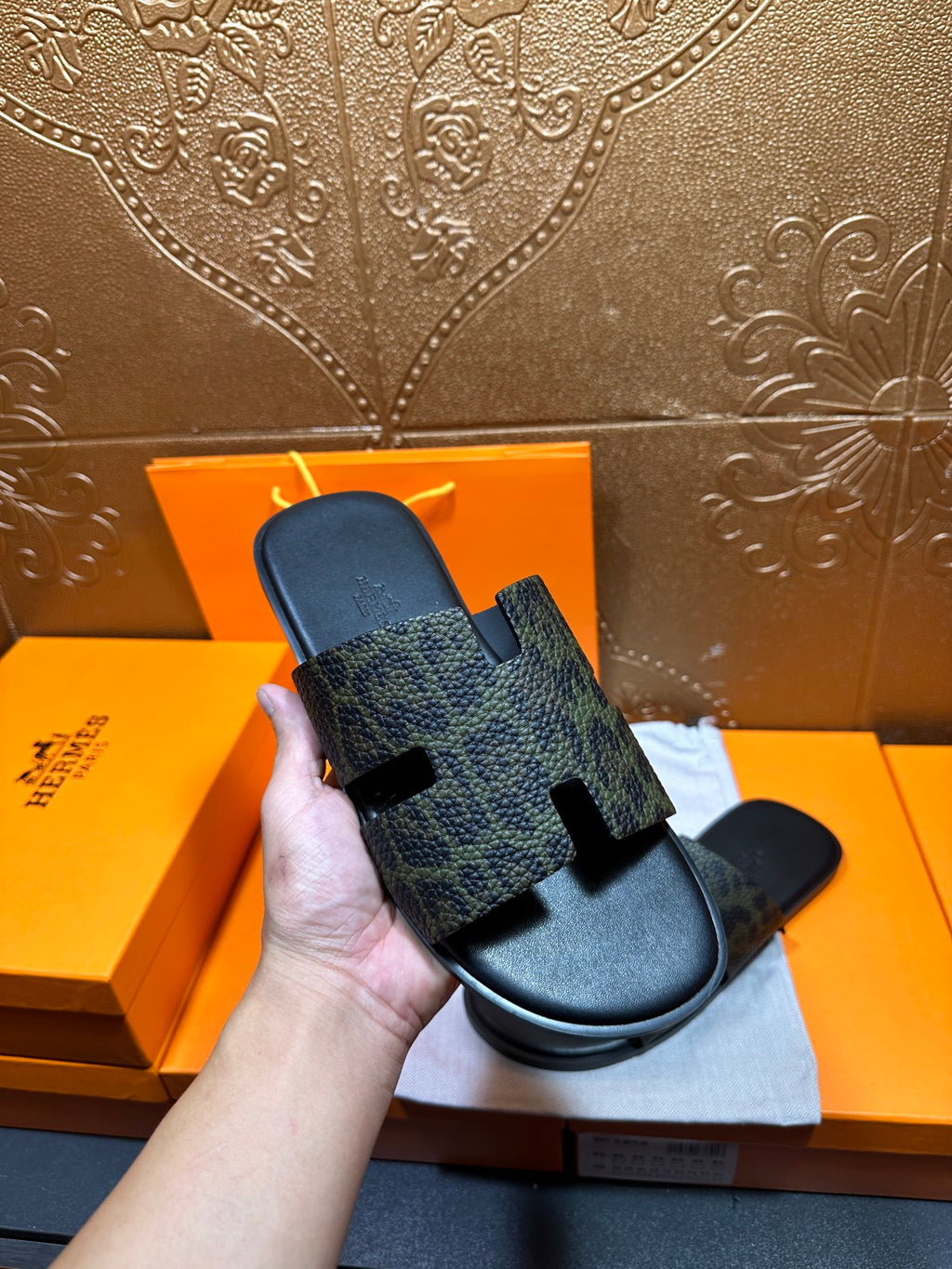 Hermes luxury slide sandals held in hand, dark patterned strap over black footbed