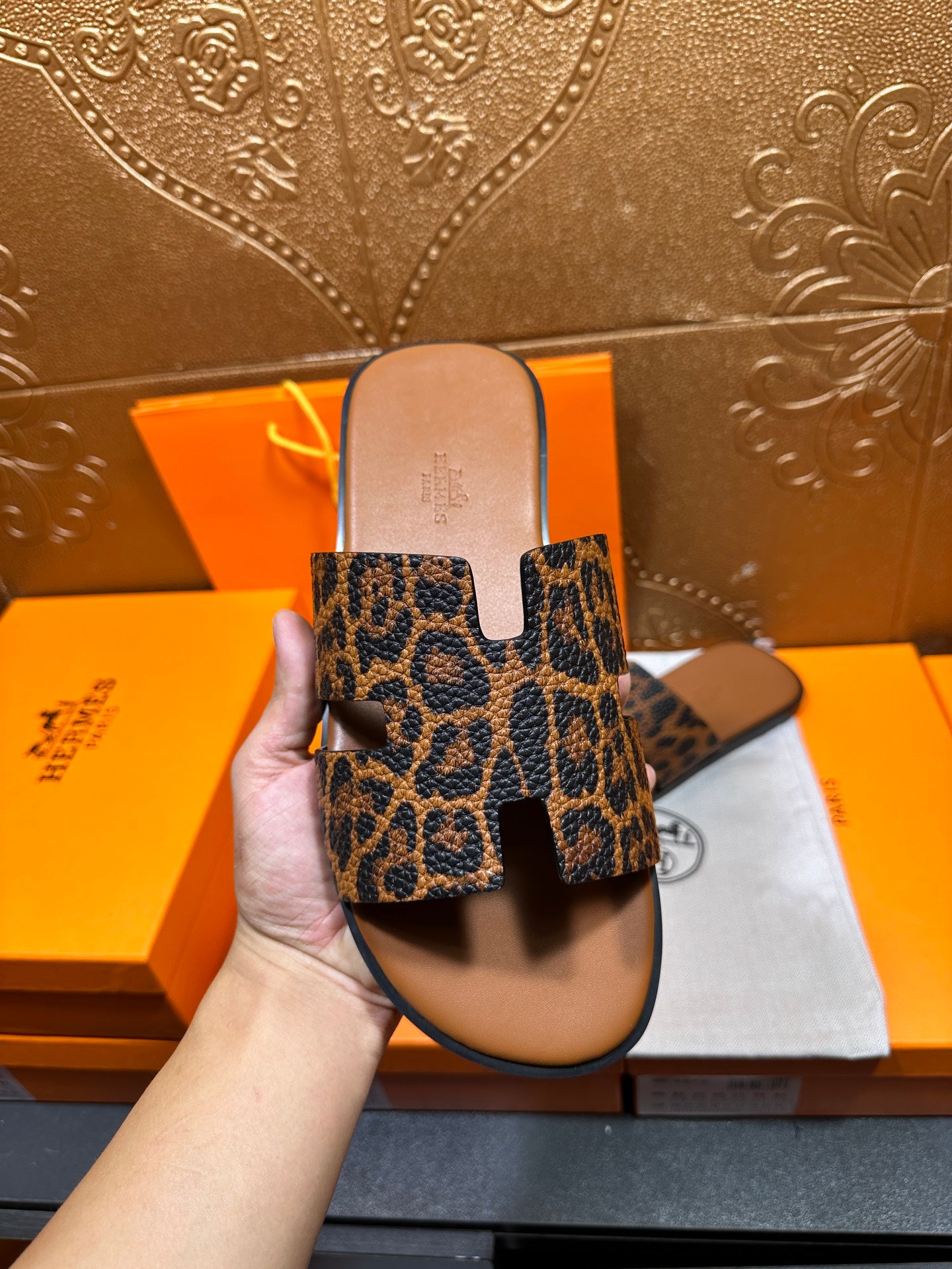 Hermes leopard-print slide sandals held up from behind, top straps visible