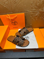 Hermes leopard-print slide sandals, angled view on a tan footbed