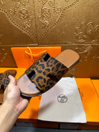 Hermes leopard-print slide sandals held up, side view of wide straps