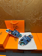 Blue denim slide sandals with colorful artwork straps, held above orange box