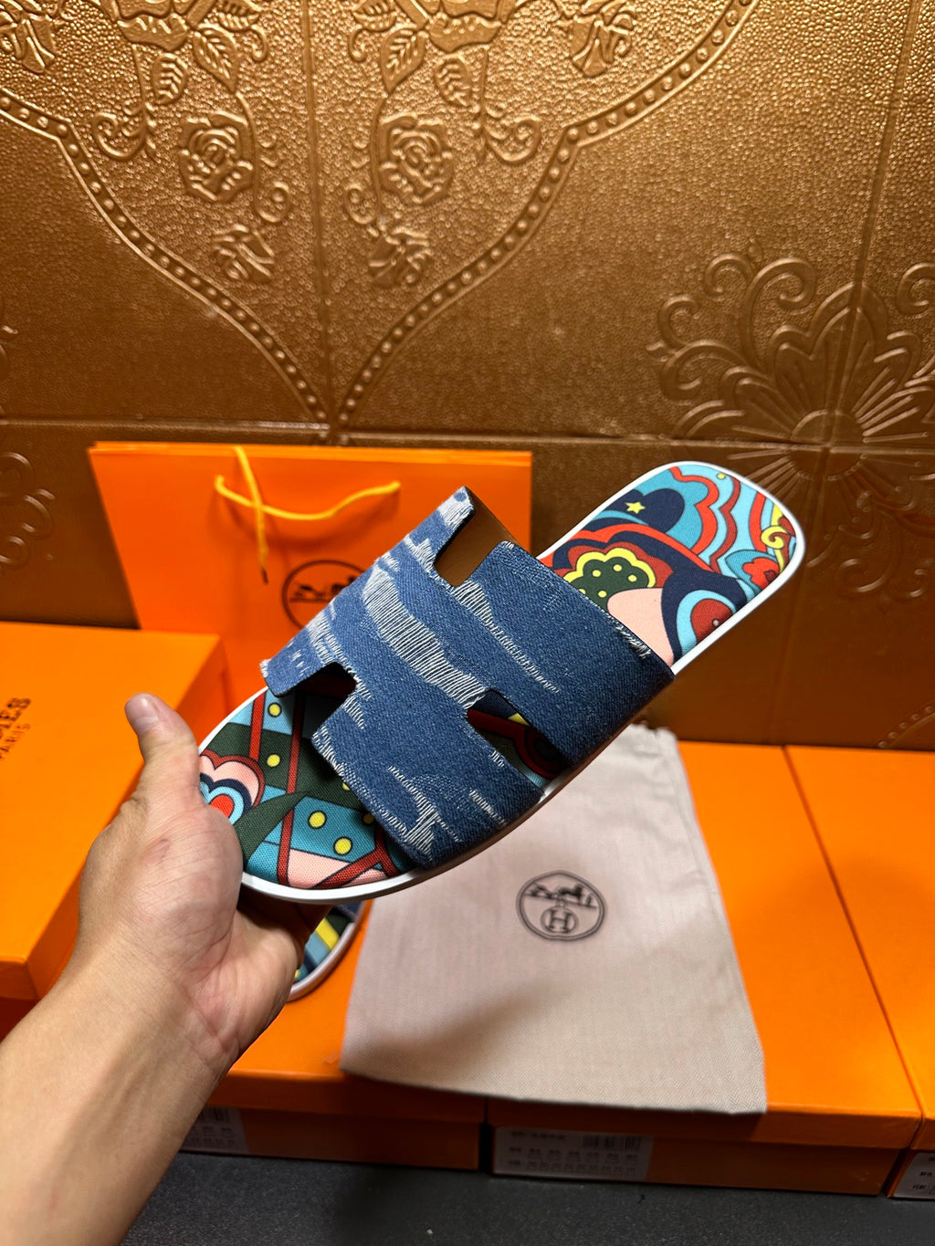Blue denim slide sandals with colorful straps, presented beside white dust bag