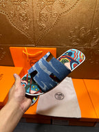 Blue denim slide sandals with colorful straps, presented beside white dust bag