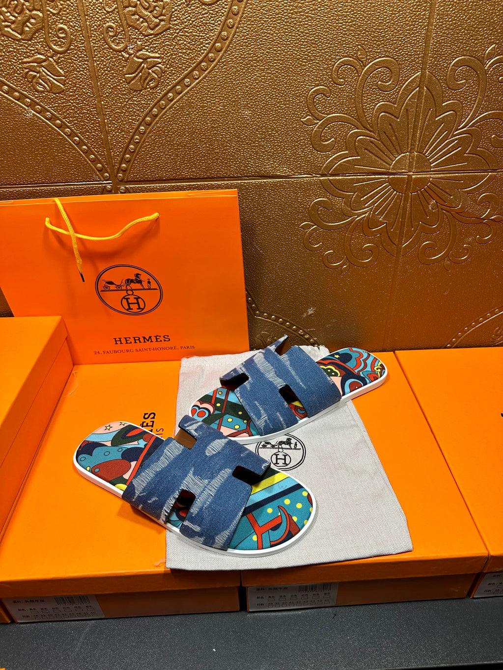 Blue denim sandals with bold colorful graphic straps, laid on storage bag
