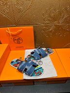 Blue denim sandals with bold colorful graphic straps, laid on storage bag