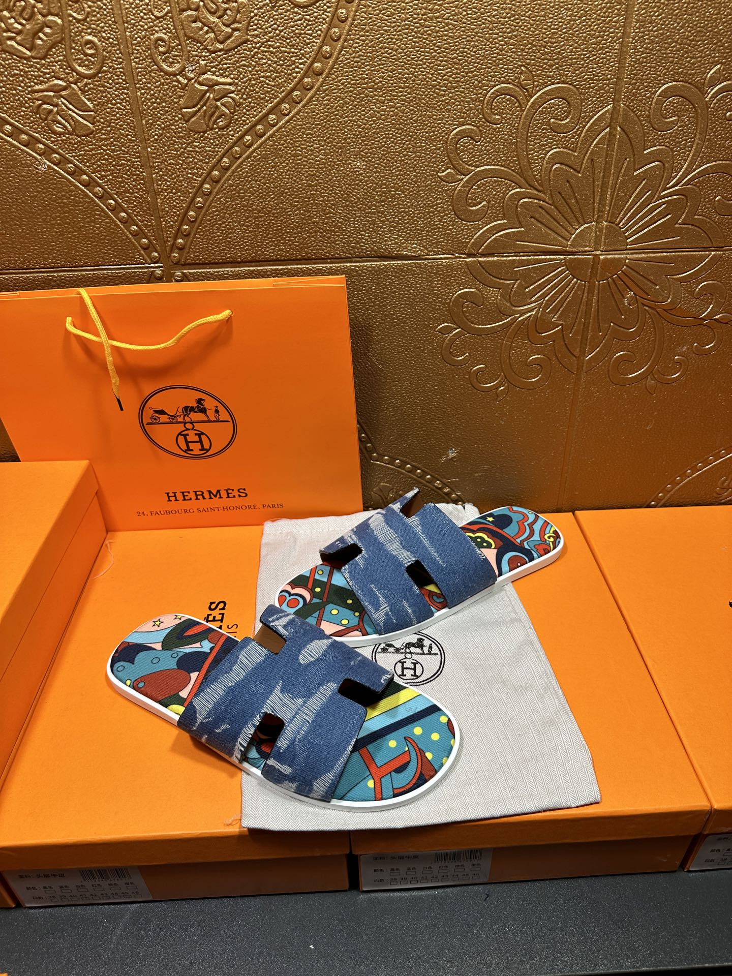 Blue denim sandals with bold colorful graphic straps, laid on storage bag