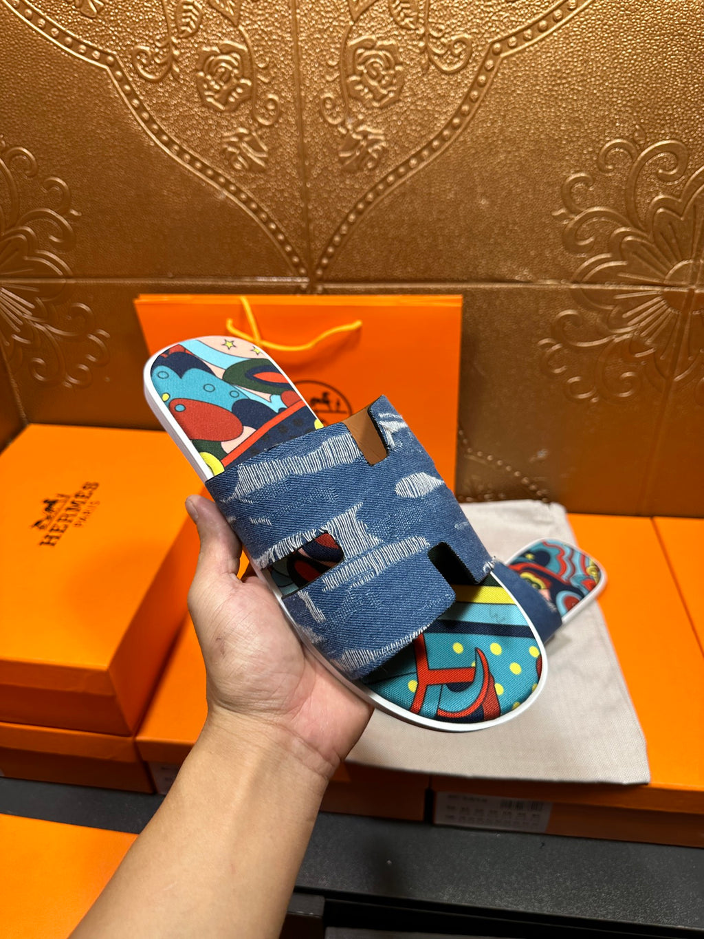 Blue denim slide sandals with colorful graphic upper, shown close to hand