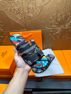 Hermes sandals held up by hand; black straps with colorful abstract print