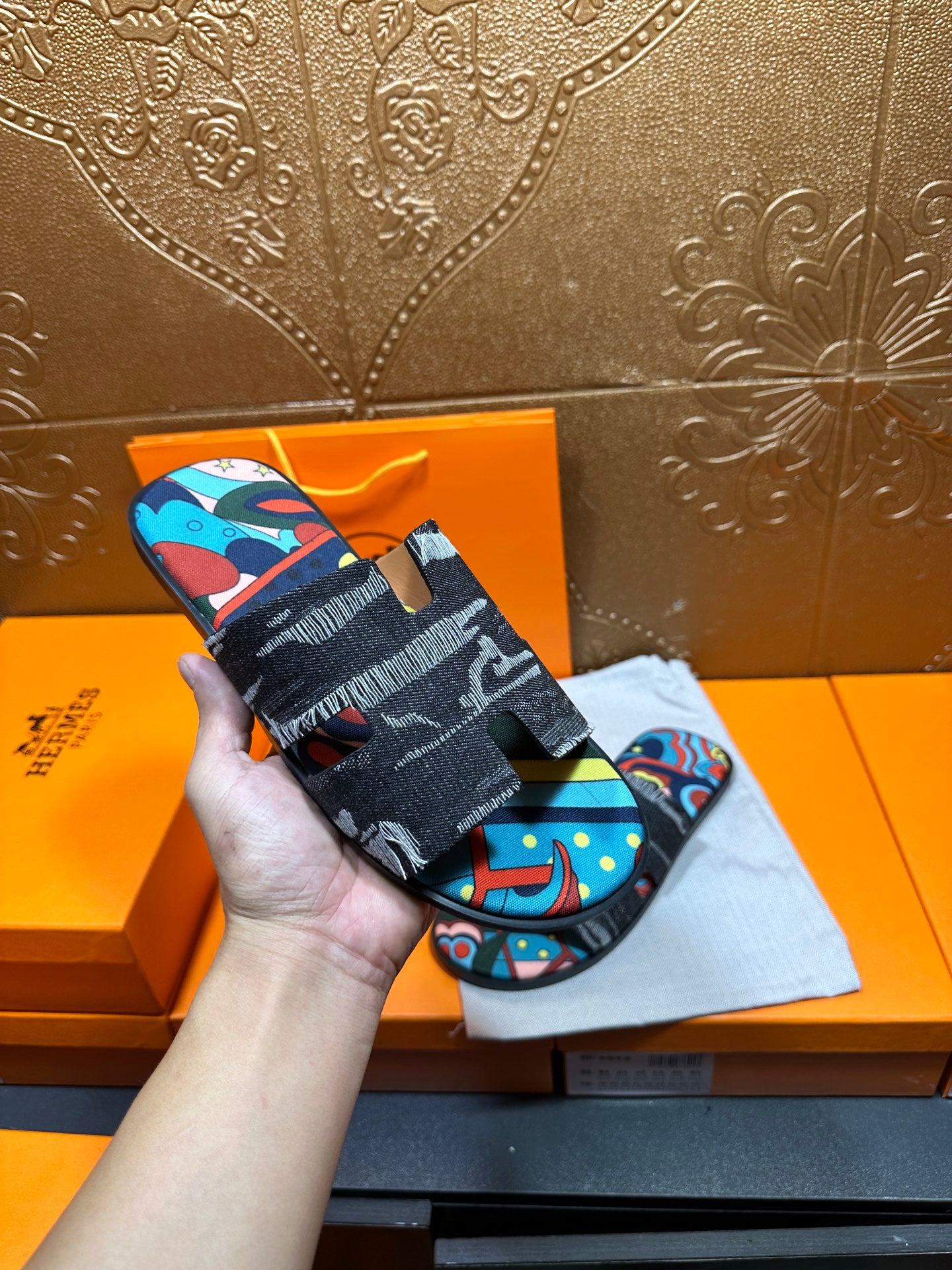 Hermes sandals held up by hand; black straps with colorful abstract print