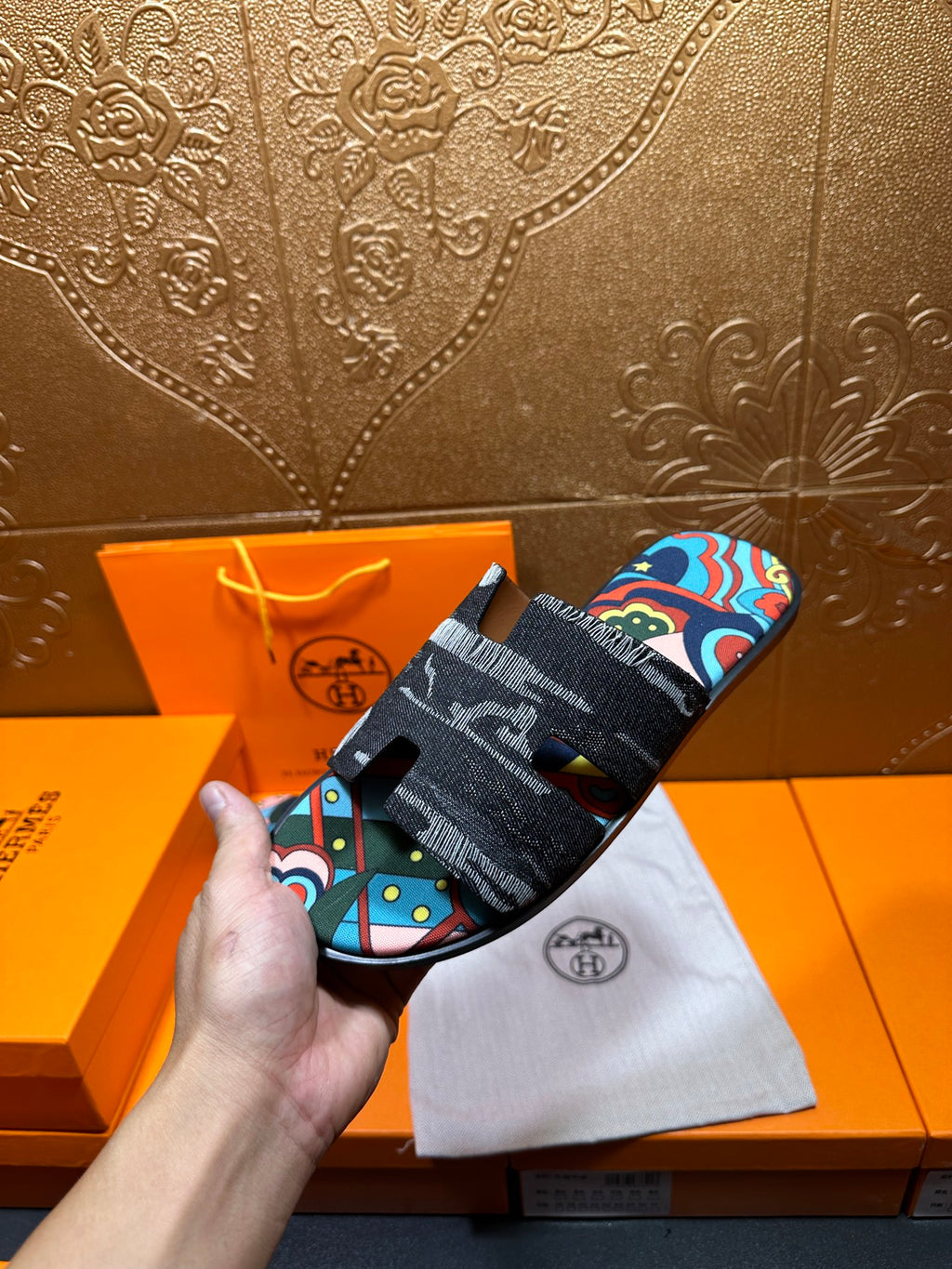 Hermes slide sandals held in hand; black straps with colorful abstract print panel