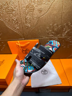 Hermes slide sandals held in hand; black straps with colorful abstract print panel