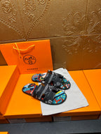Hermes sandals resting on a fabric bag; black straps with colorful geometric print