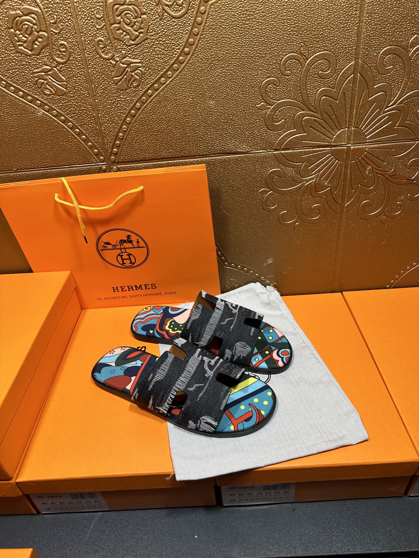 Hermes sandals resting on a fabric bag; black straps with colorful geometric print