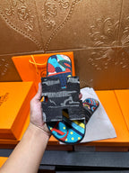 Hermes sandals held in hand; black textured straps with colorful abstract top