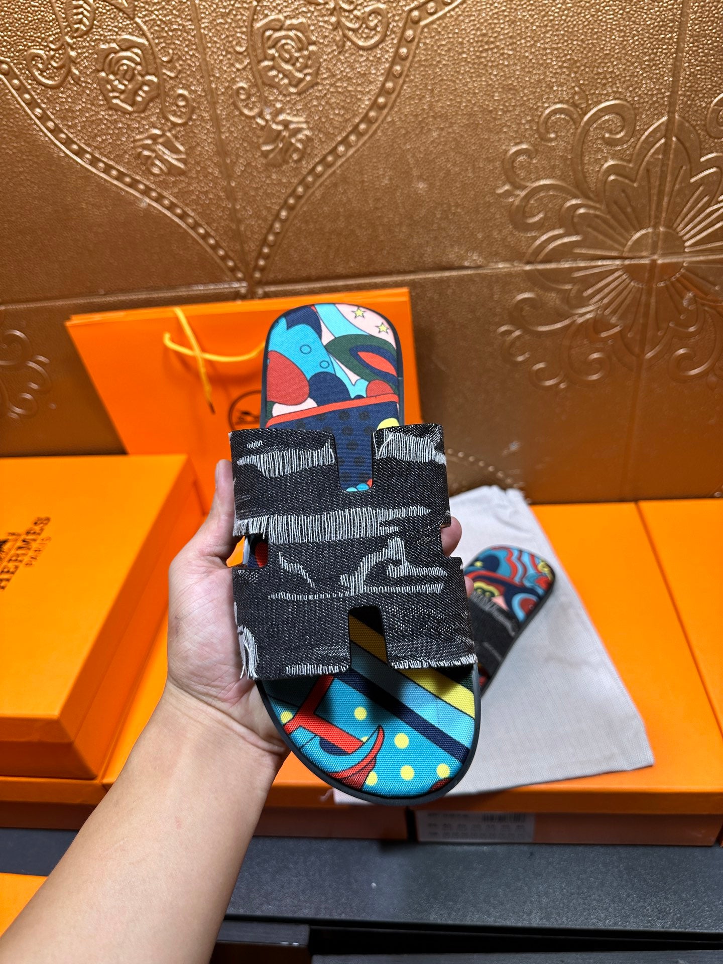 Hermes sandals held in hand; black textured straps with colorful abstract top