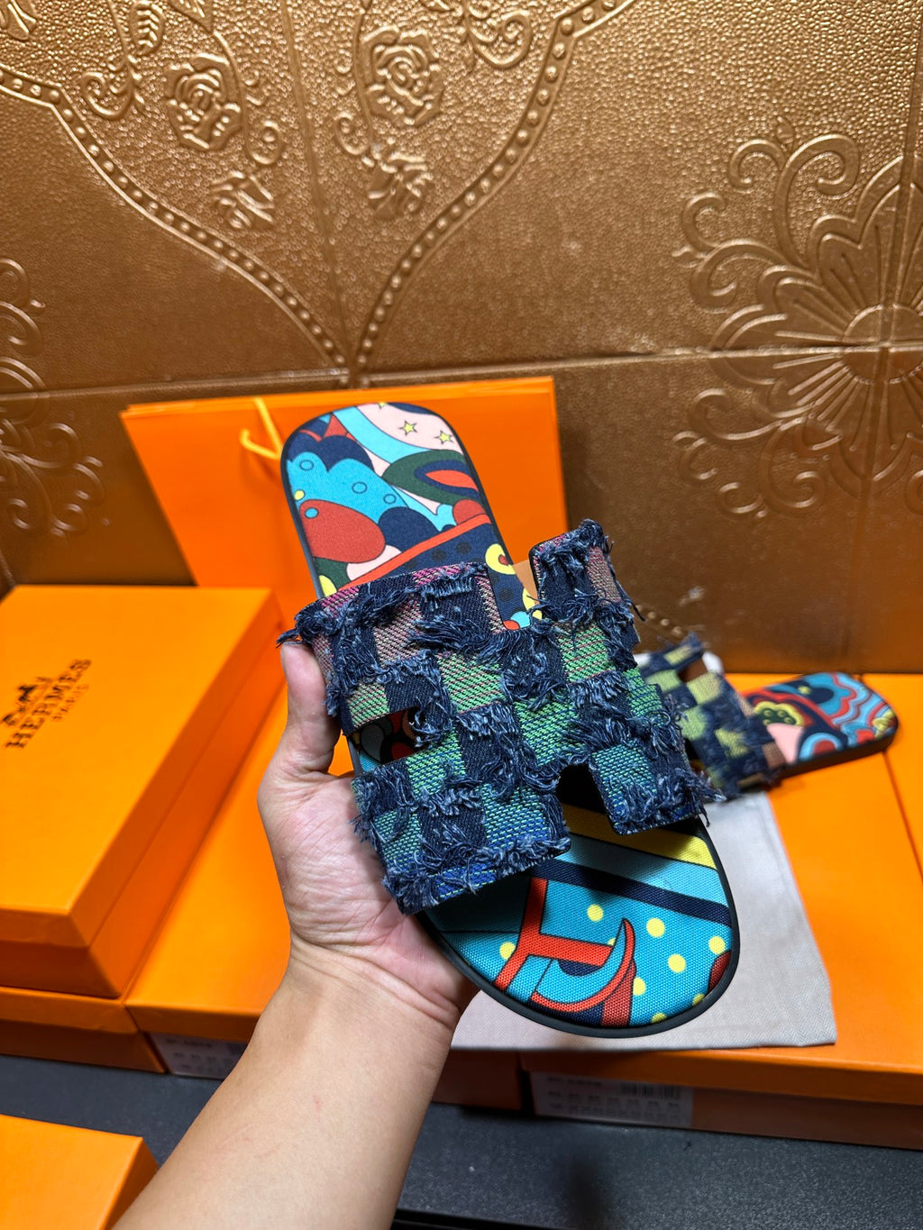 Hand holding blue patterned slide sandals with frayed ankle wrap and colorful print