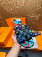 Hand holding blue patterned slide sandals with frayed ankle wrap and colorful print