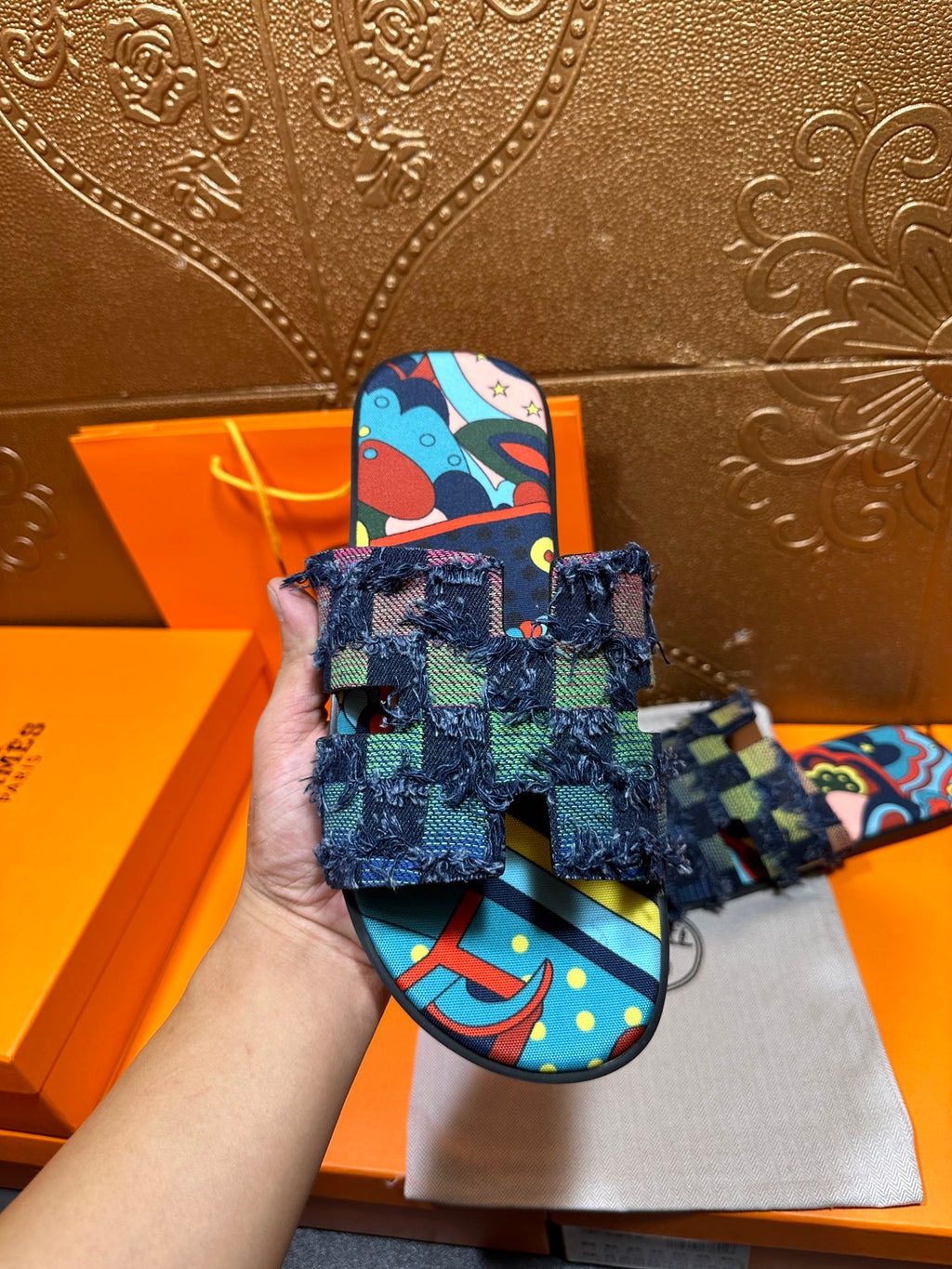 Blue patterned slide sandal held up, showing frayed ankle wrap and toe strap