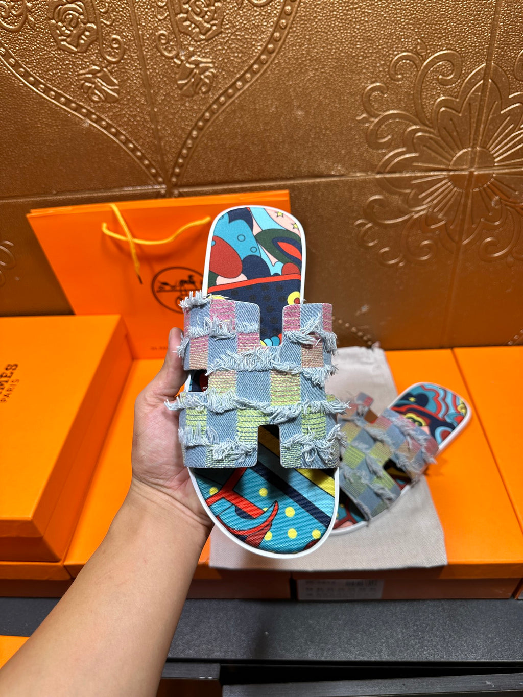 Hermes patchwork slide sandals held in hand, multicolor fabric straps with graphic pattern