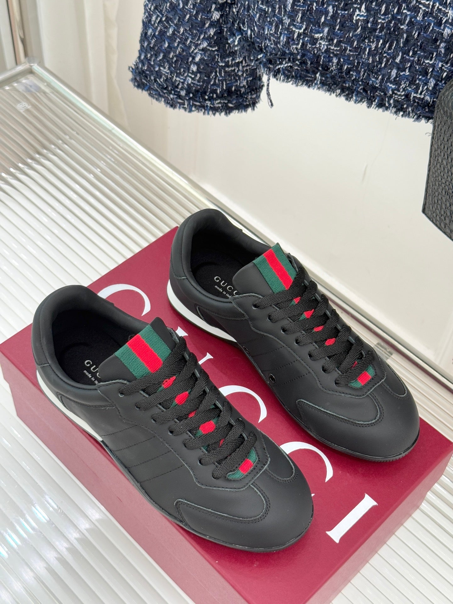 Pair of black leather sneakers on a box, with red and green stripe accents